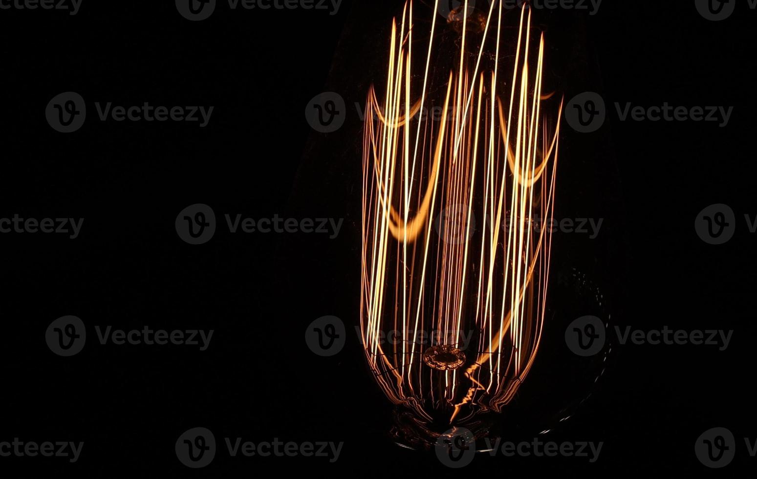 close up of retro light bulb on black background. Tungsten filaments glow with a warm orange light. The spiral vibrates with electricity. photo