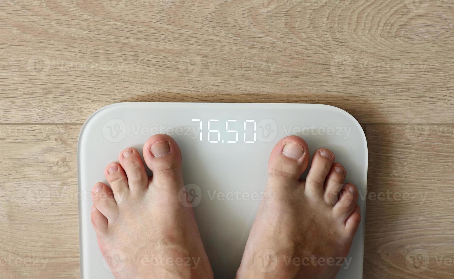Man weighing himself  male bare feet stepping on white digital floor scales at home close up view. Measuring weight, control, wellness and diet concept photo