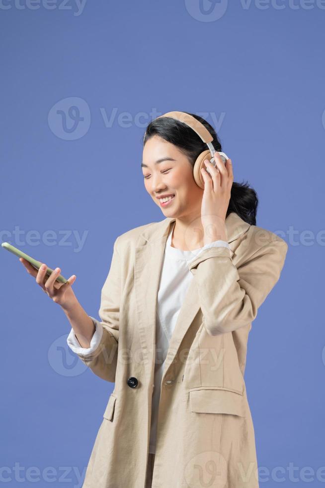 Half length of smiling young lady with earbuds looking away while holding mobile phone in arm photo