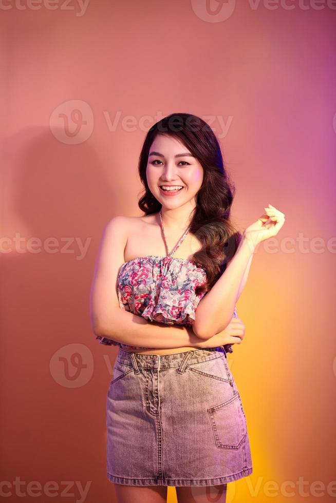 Smiling, looks dreamful. Attractive woman's portrait isolated on orange studio background in mixed neon light. photo