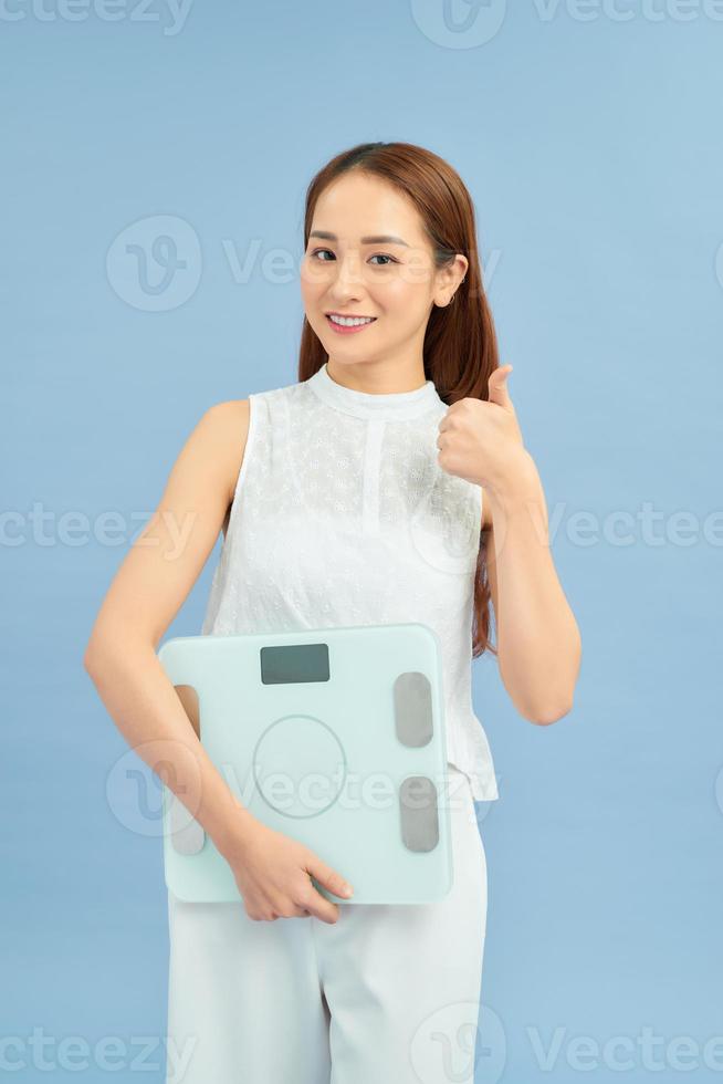 Young woman holding scale for healthy weight happy with big smile doing ok sign, thumb up with fingers, excellent sign photo