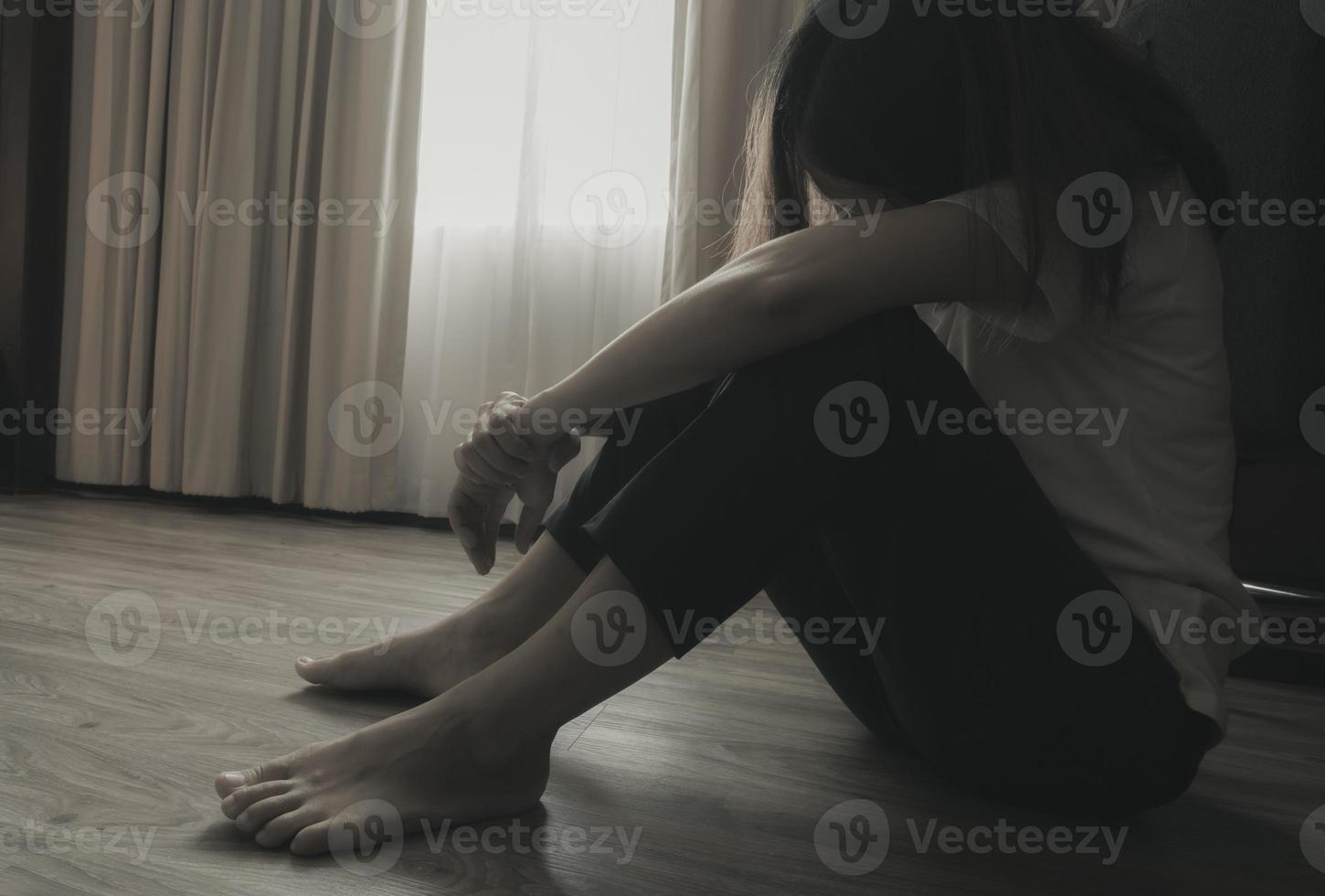 mujer deprimida y estresada sentada en el suelo cerca de las cortinas en el dormitorio. mujer triste sentada en el cuarto oscuro. niña con problemas de salud mental. vida infeliz concepto del día mundial de la salud mental. foto