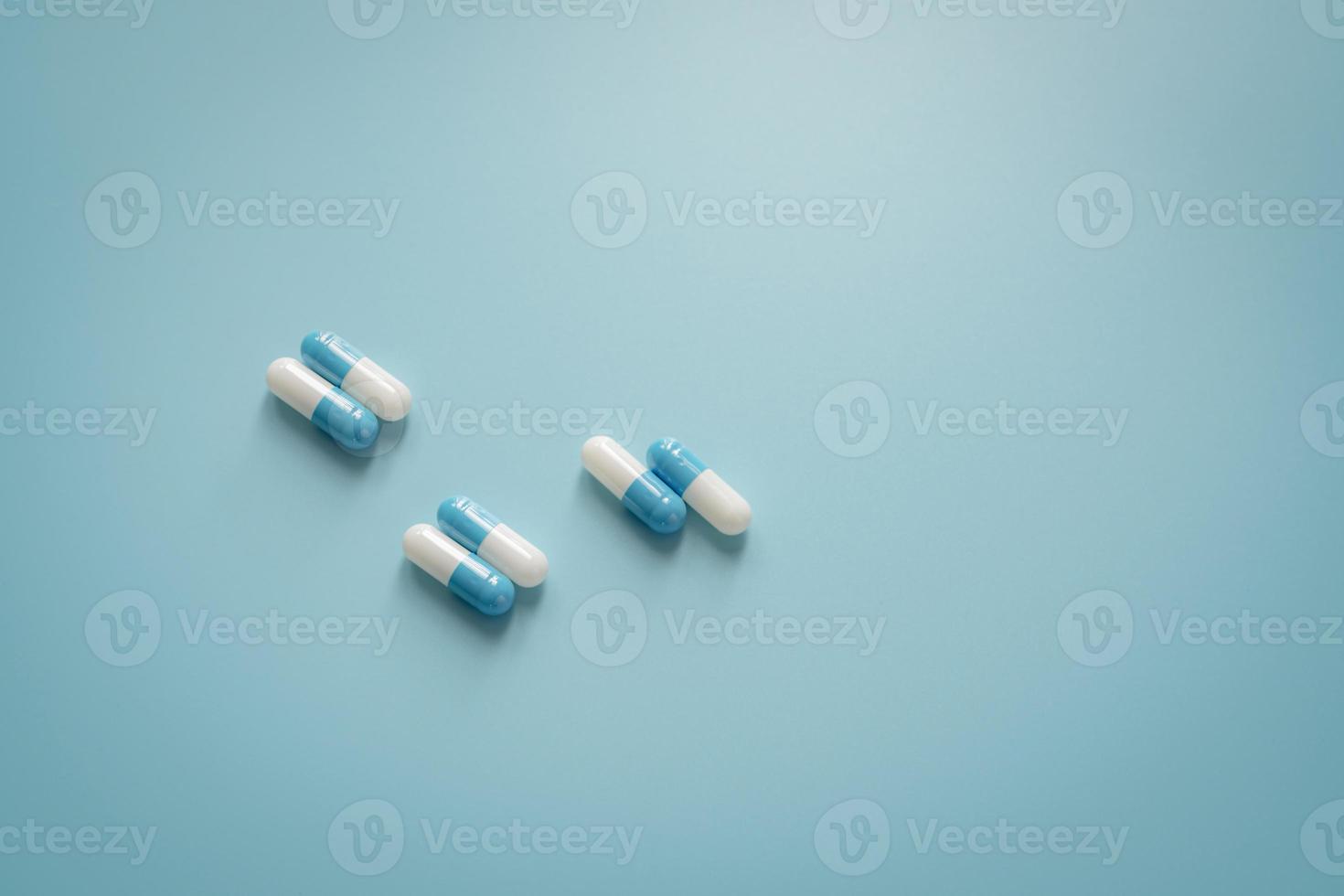 Pairs of white-blue antibiotic capsule pills on blue background. Antibiotic drug. Prescription drug. Pharmacology and recommended dose concept. Pharmaceutical industry. Medical and healthcare concept. photo