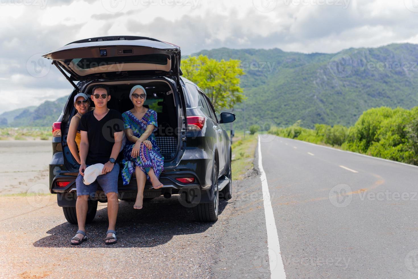 Portrait of three people sitting on back of a truck in countryside road trip. photo