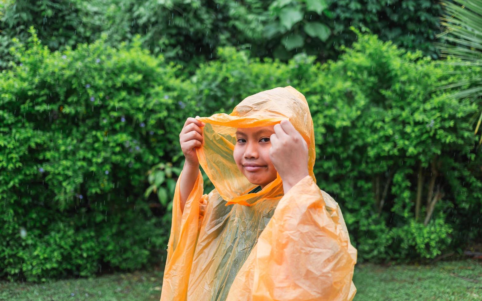 un niño asiático con impermeable naranja es feliz y se divierte bajo la lluvia en un día lluvioso. foto