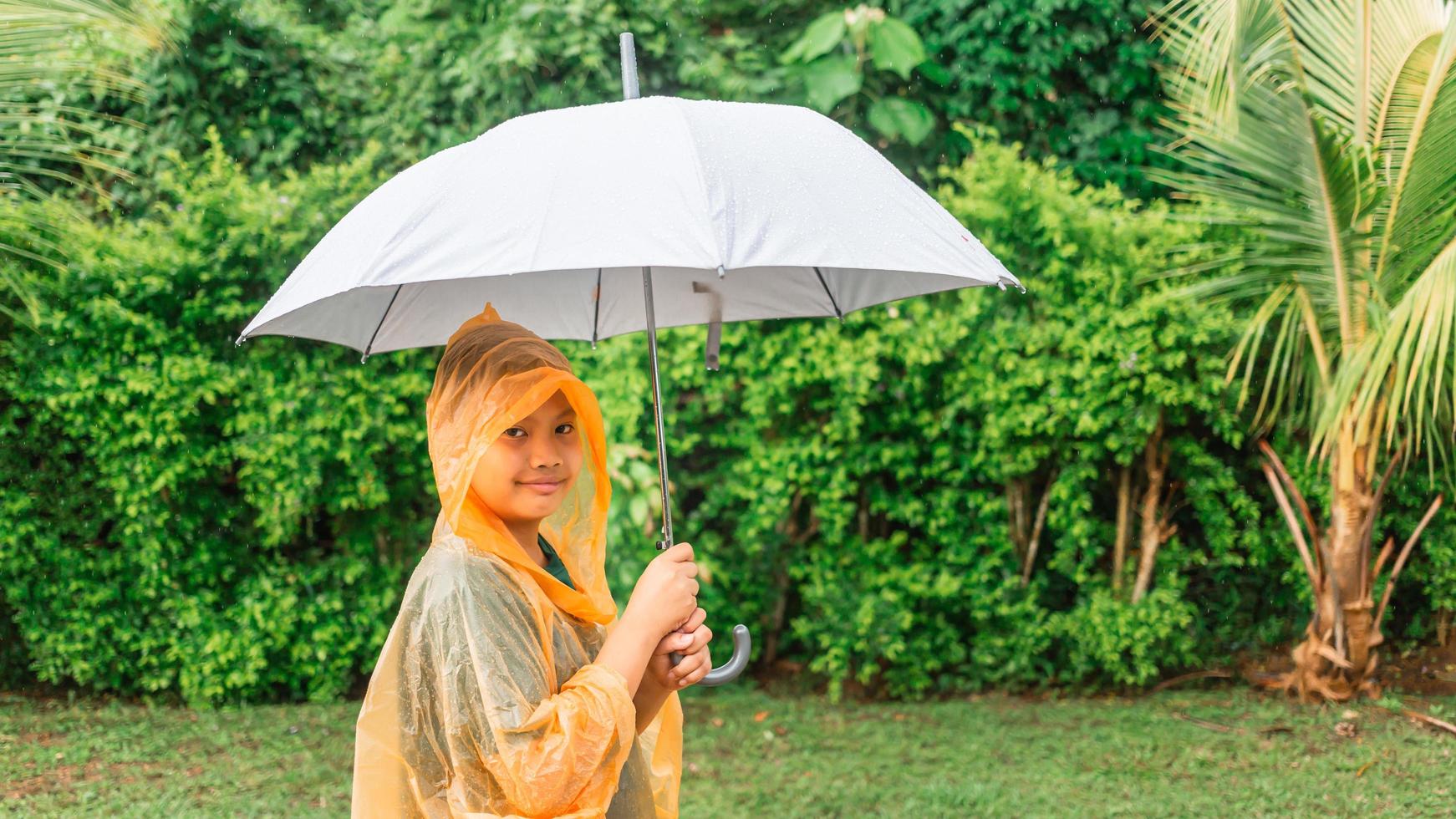 Asian boy puts on a raincoat and opens an umbrella on a rainy day. photo
