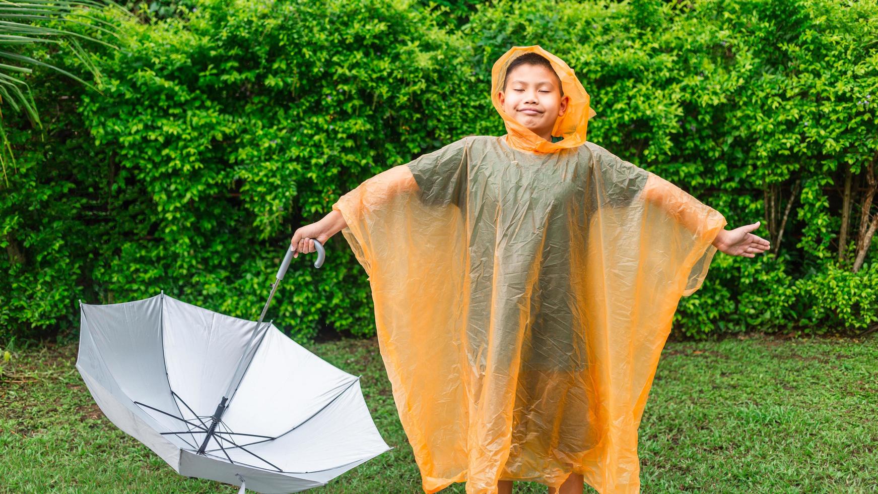 Asian boy wearing orange raincoat holding umbrella happy and having fun in the rain on a rainy day photo