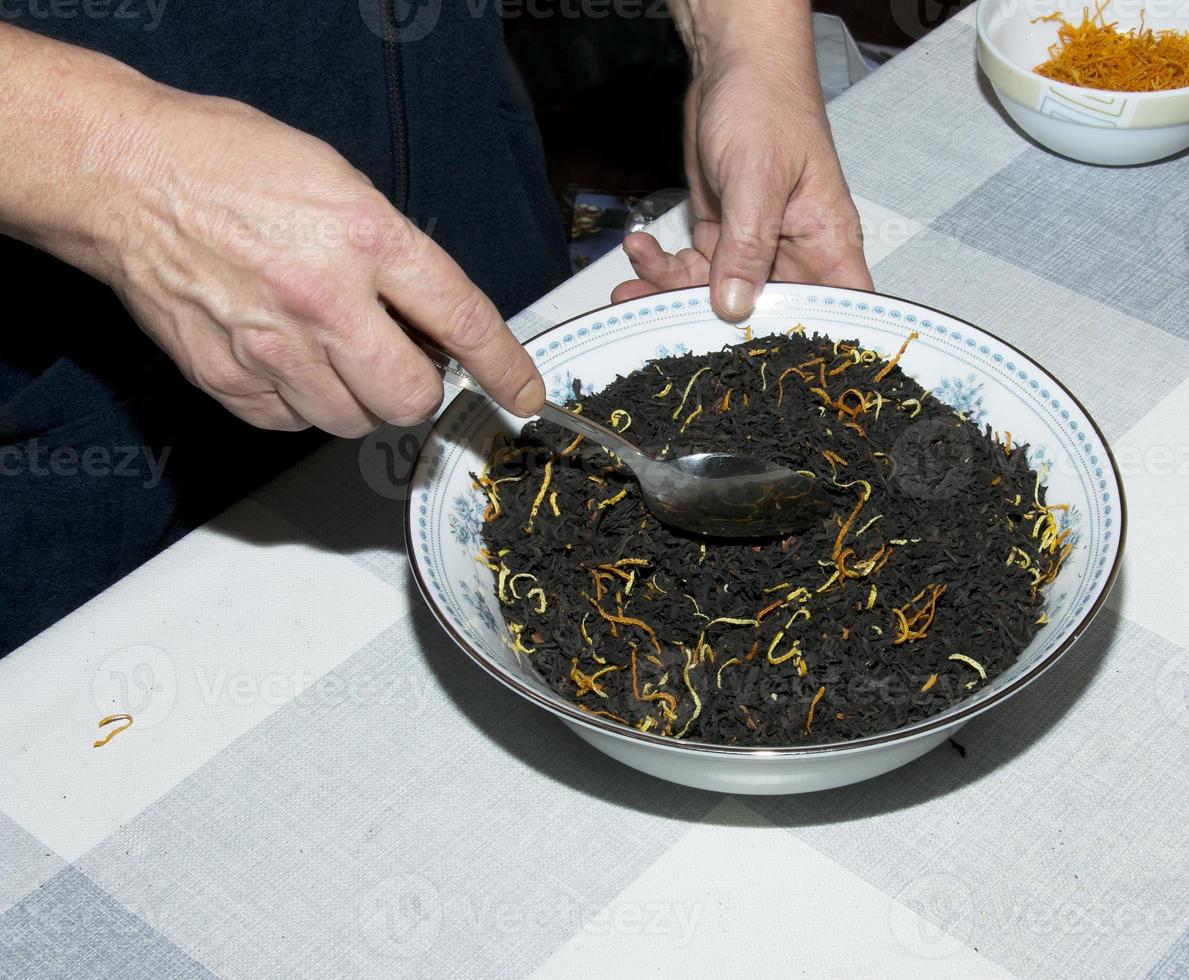 Female hands stir the tea mixture with a spoon. The process of making tea from black tea, lemon and orange peel, pieces of cinnamon sticks. photo