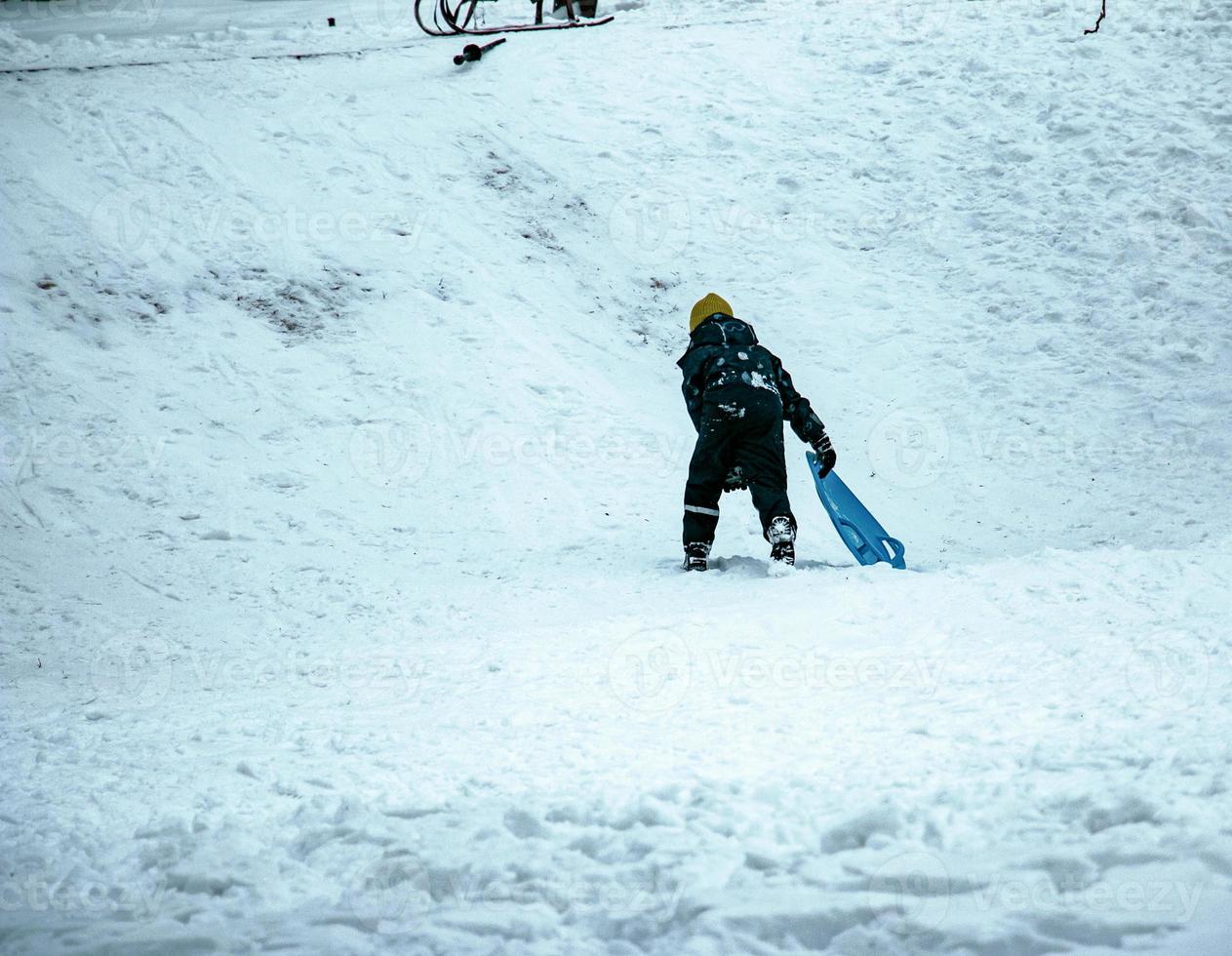 Little boy sledding downhill in winter. The boy falls into the snow. Outdoor play for children. Children's sledges in a snow-covered park. photo