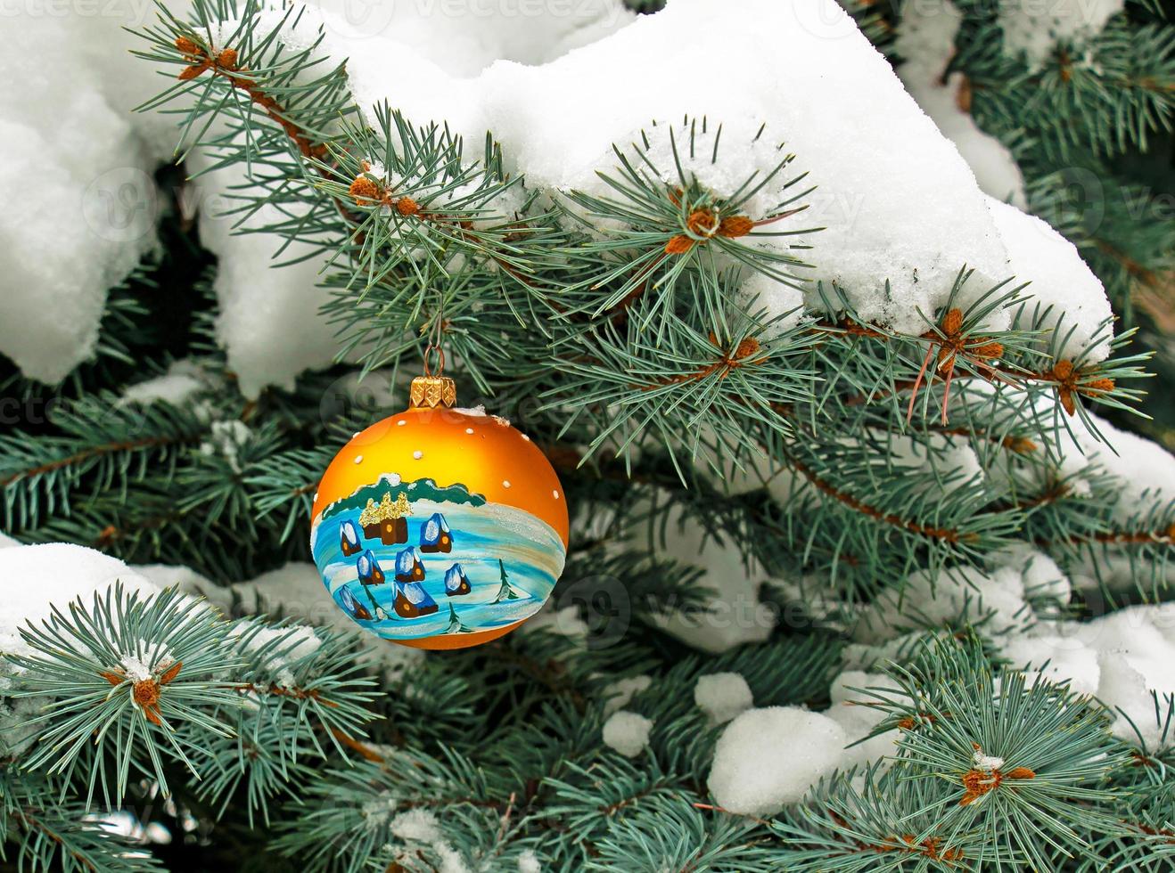 Christmas ball hanging on a snow-covered branch of a Christmas tree on a festive background of white snow and snowy bokeh with copy space. photo