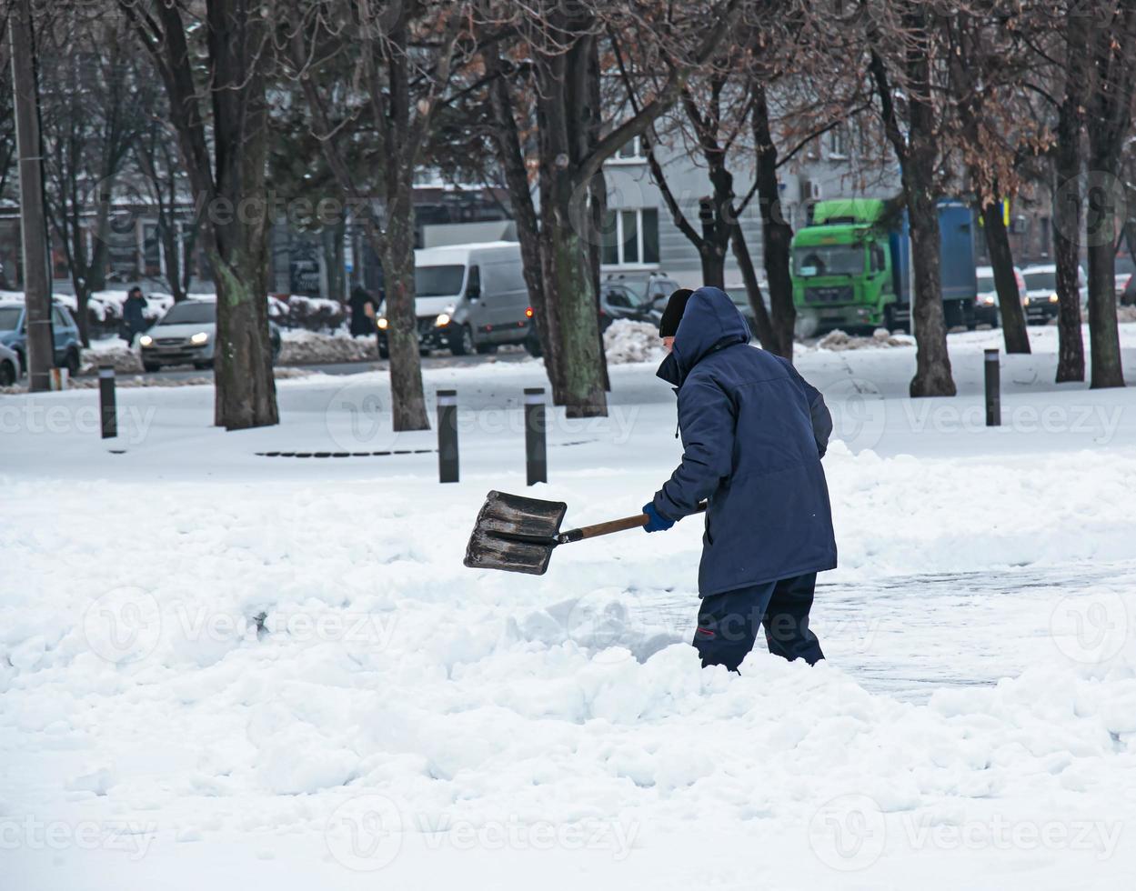 Man with a shovel clears snow outdoor. Worker during snow removal in winter city, street cleaning photo