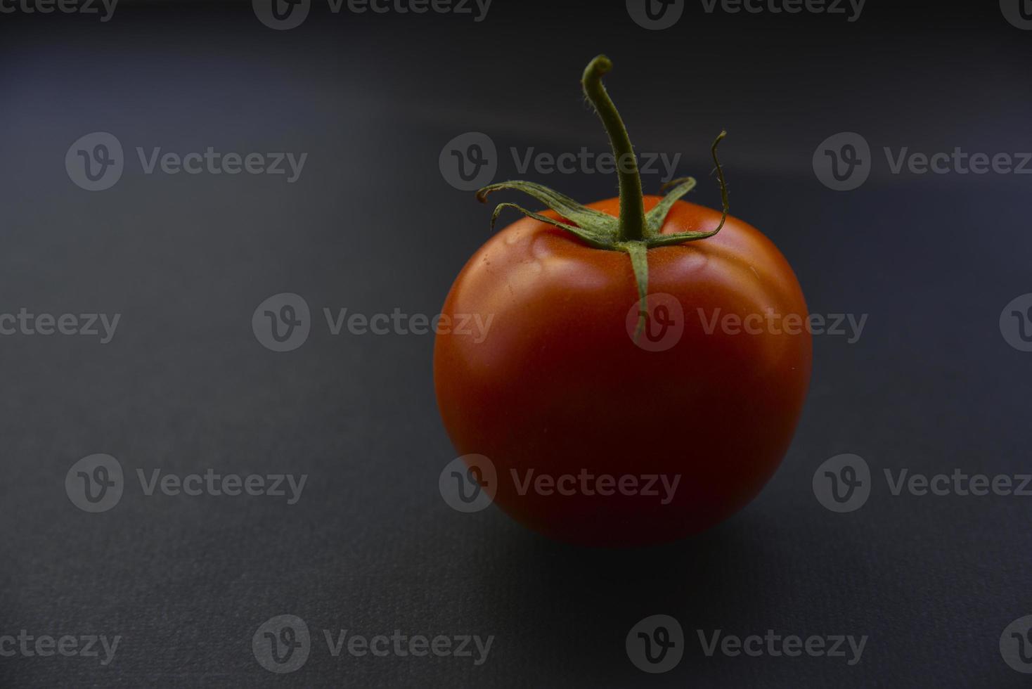 tomate fresco rojo sobre un fondo negro. primer plano de una fruta de tomate. foto