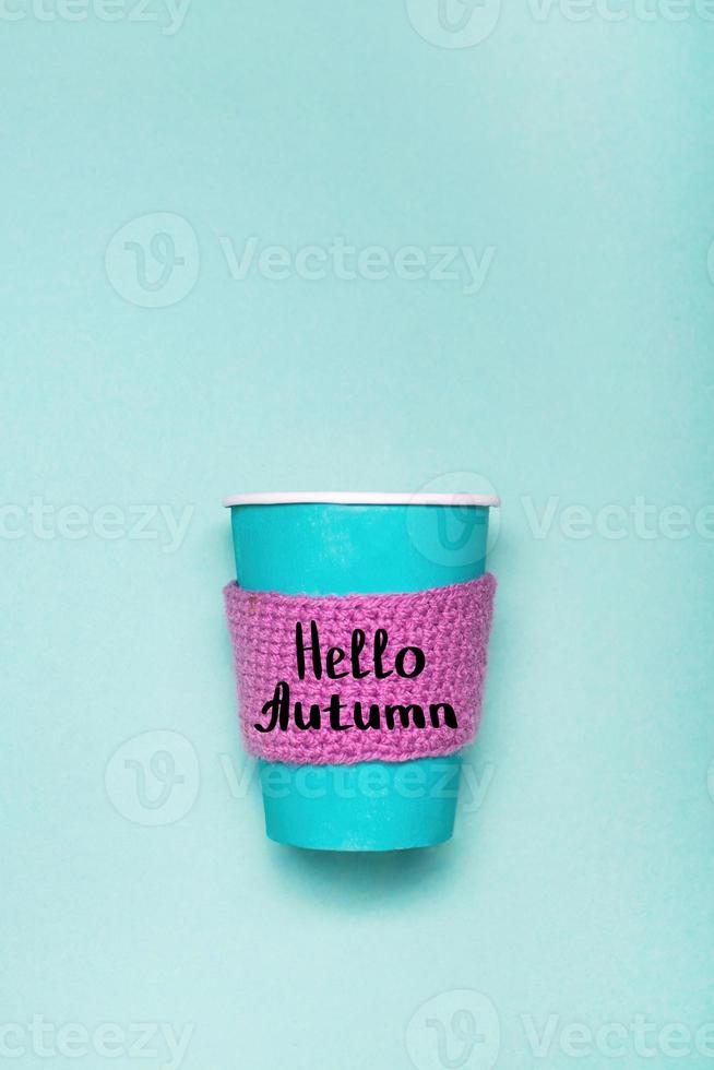 Mockup of coffee paper cup on a green background. Cozy coffee paper cup with knitted scarf and lettering Hello Autumn. photo