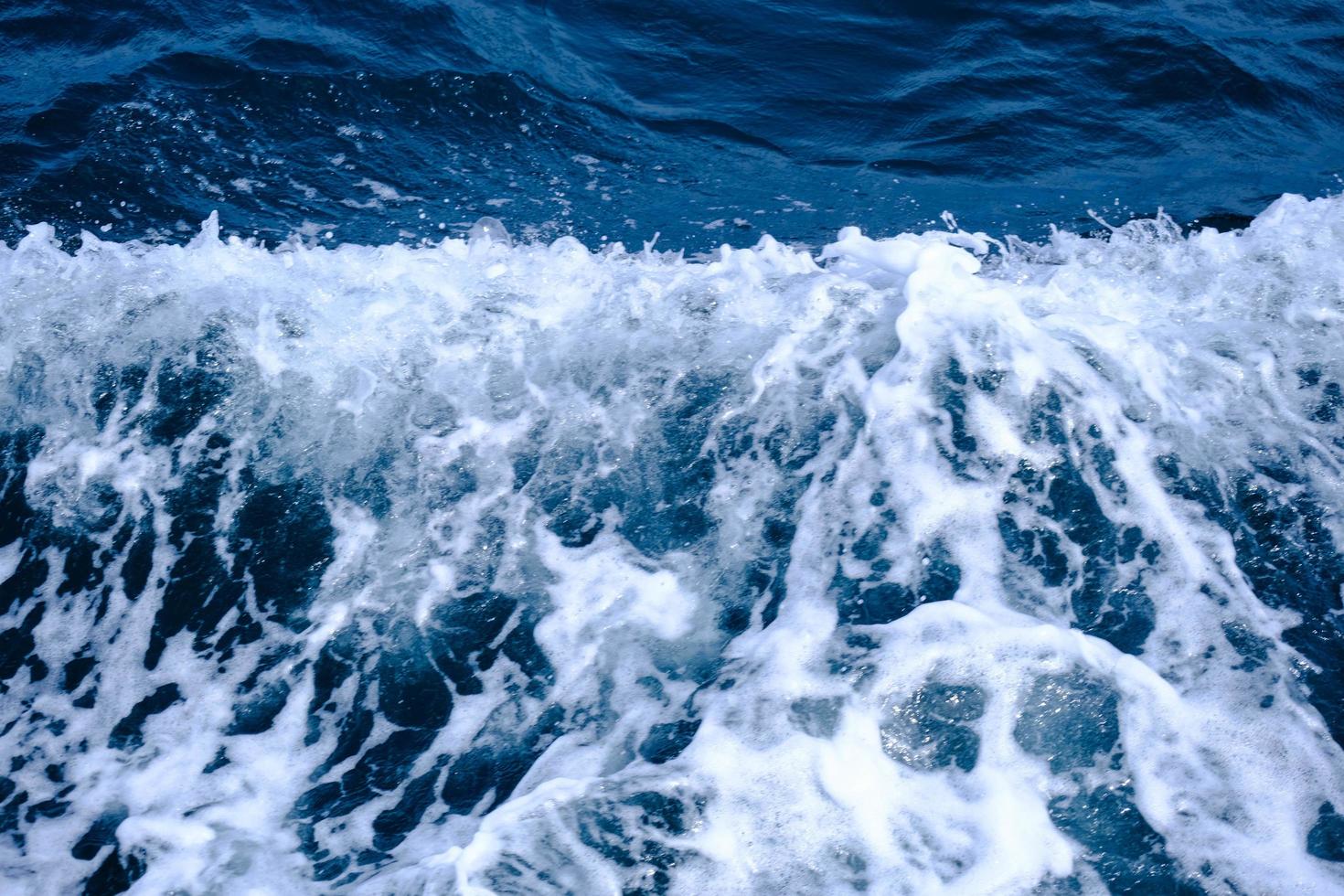 las olas al lado del barco navegan en el mar en verano. fondo de olas azules del océano y burbujas de espuma blanca. foto