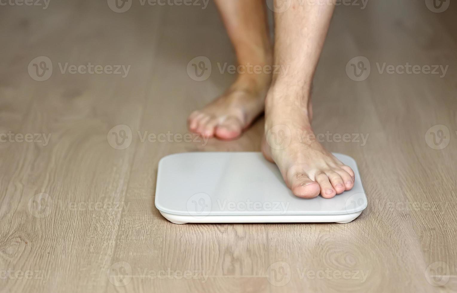 Man walking on scales measure weight. male wal checking BMI weight loss. human barefoot measuring body fat overweight. Guy legs step on bathroom scale photo