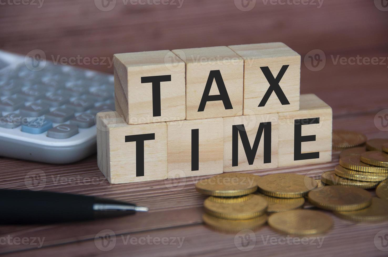 Tax time text on wooden blocks with gold coins, pen and calculator. Tax concept photo