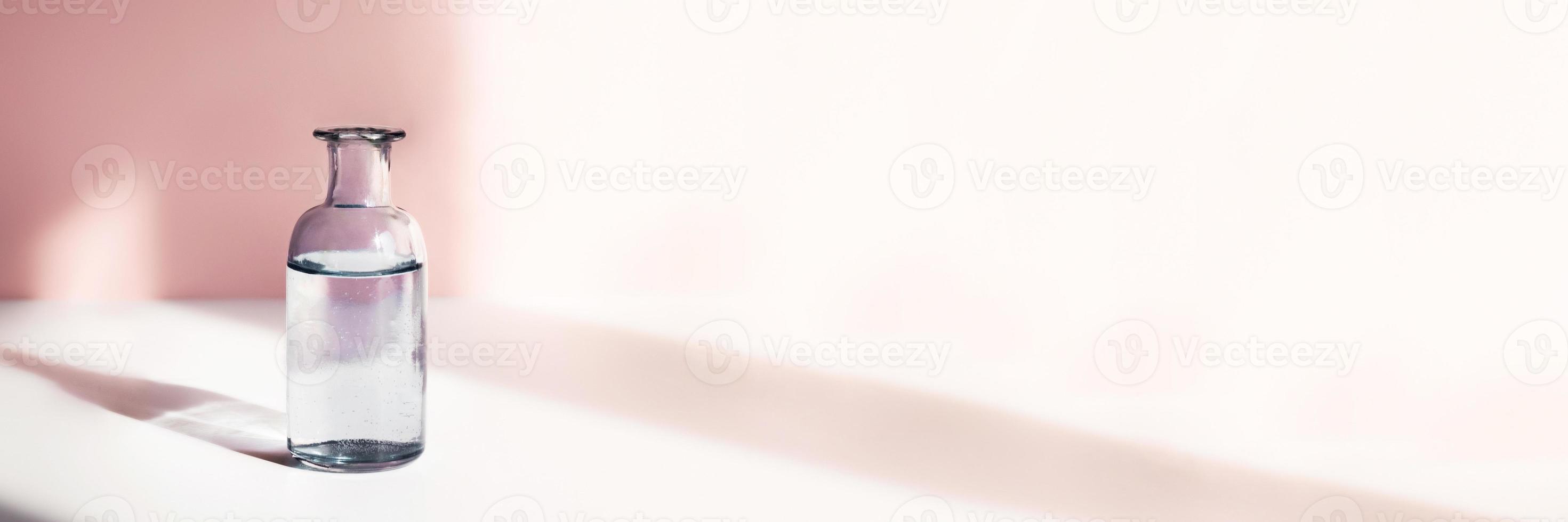Glass vase with water for flowers in sunlight on pink background. Cute web banner in pastel-colored with place for text. photo