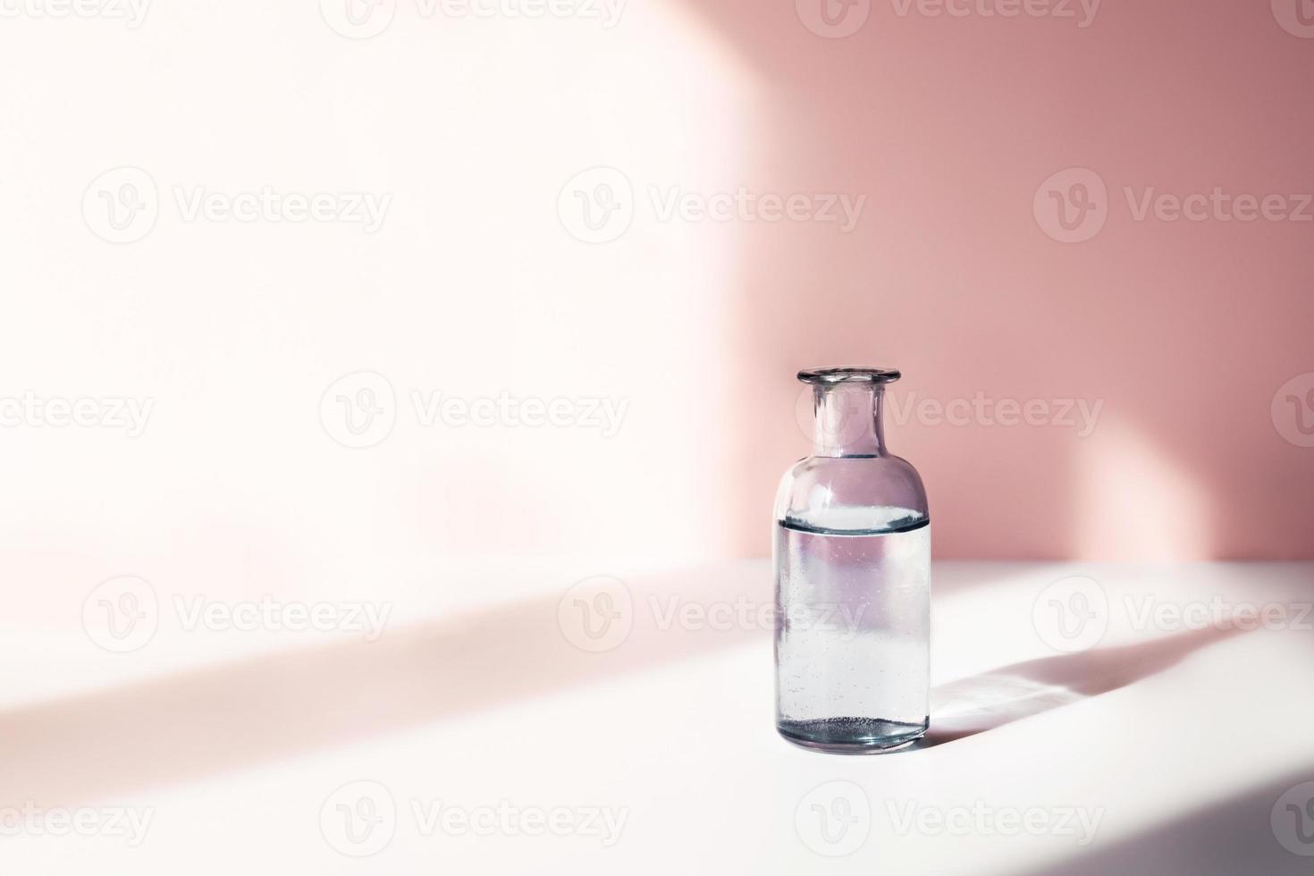 Glass vase with water for flowers in sunlight on pink background. Cute picture pastel-colored with space for text. photo