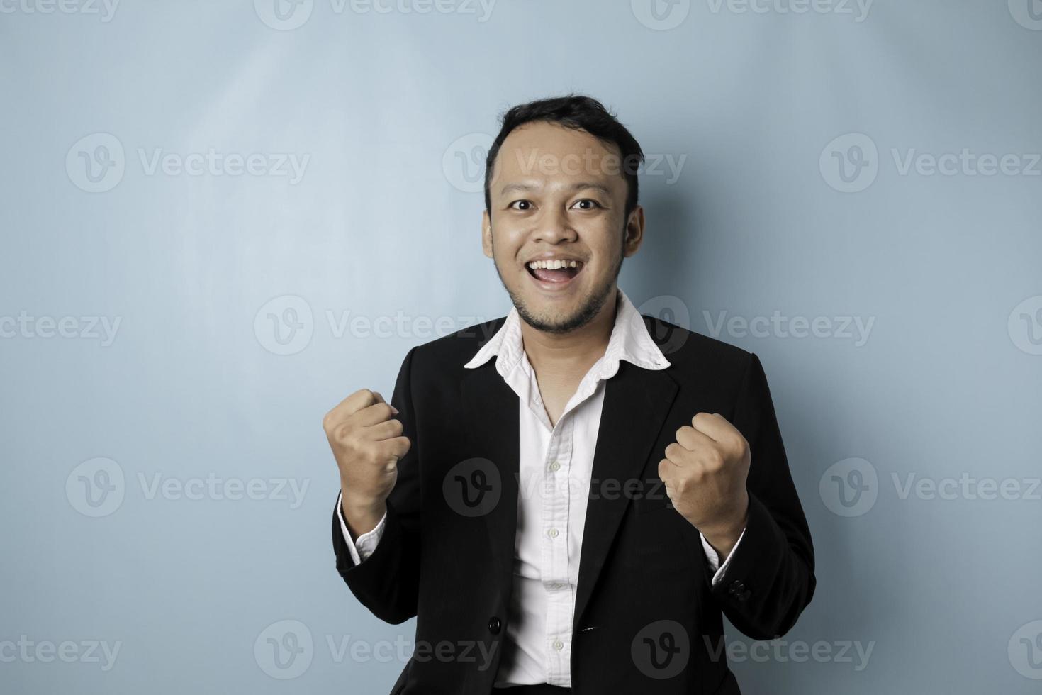 A young Asian man with a happy successful expression wearing suit isolated by blue background photo