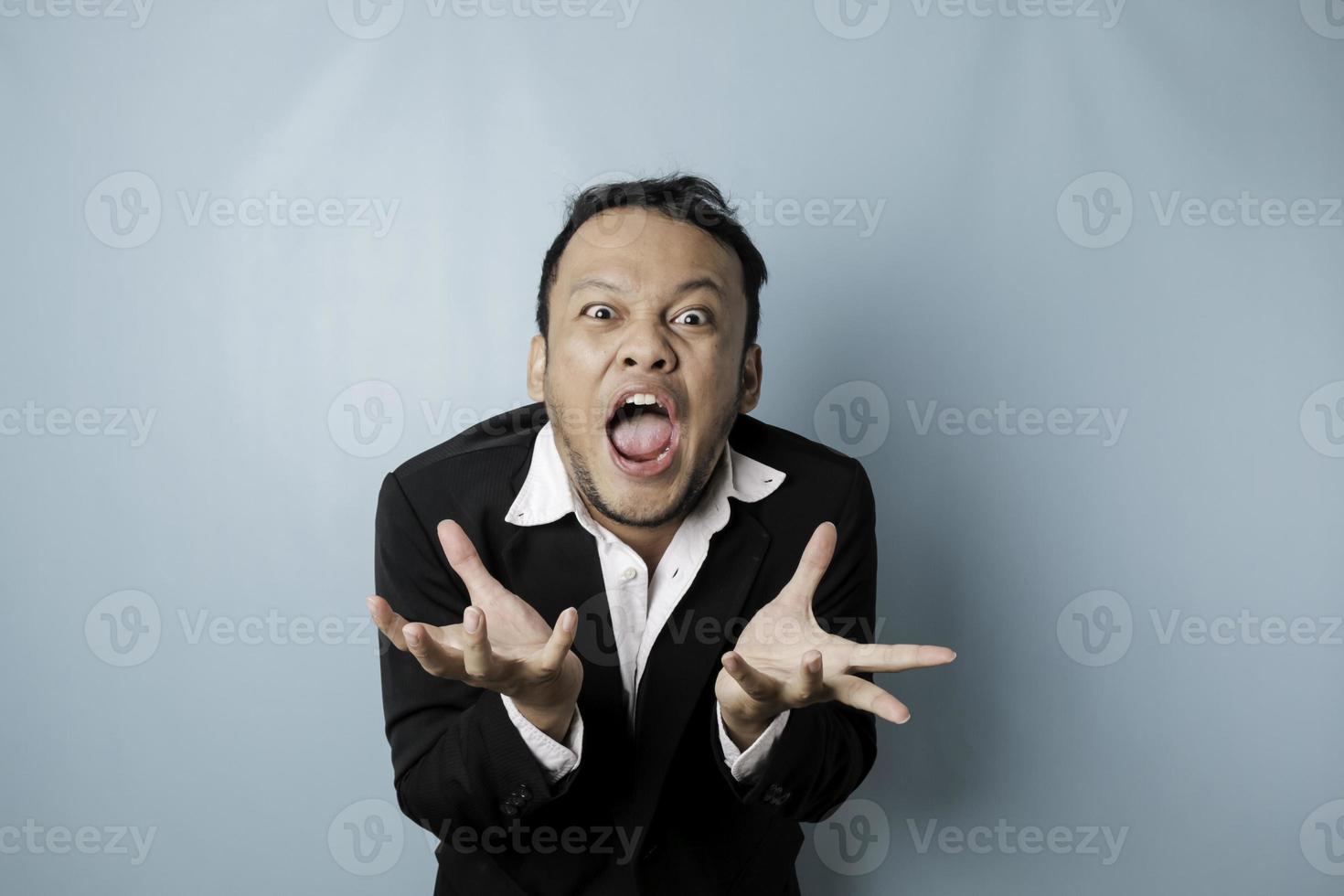 Angry and mad face of Asian businessman in black suit on isolated blue background. photo