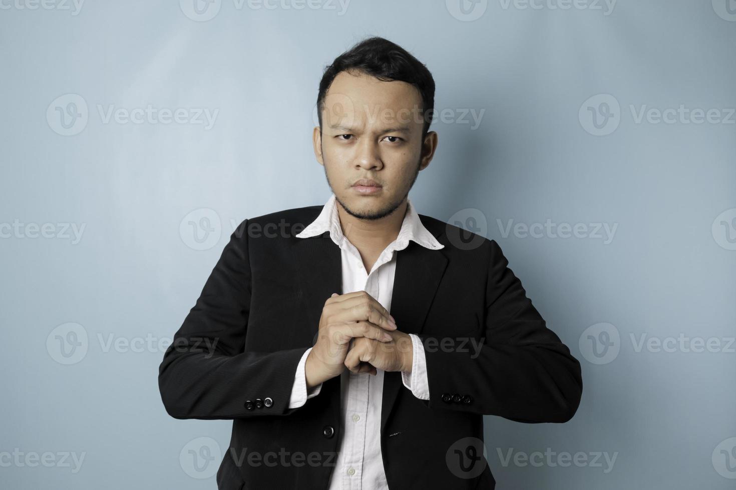 un retrato de un joven hombre de negocios asiático se ve enojado y sostiene su puño listo para golpear, aislado por un fondo azul foto