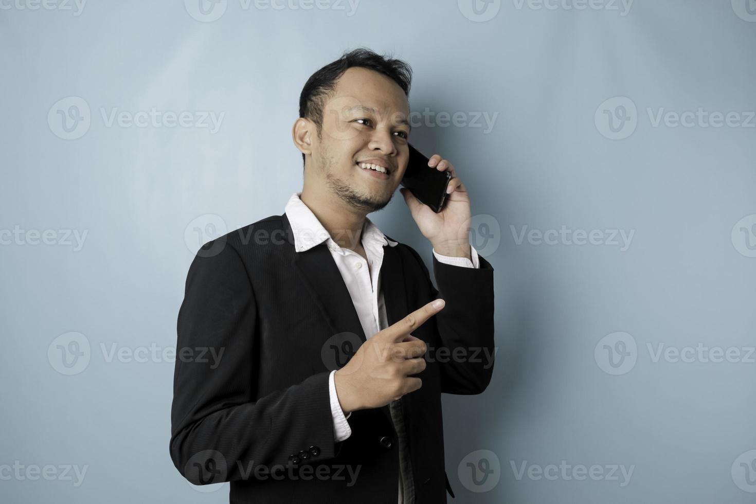 retrato de un hombre de negocios asiático con un traje negro sonriendo mientras habla por teléfono foto