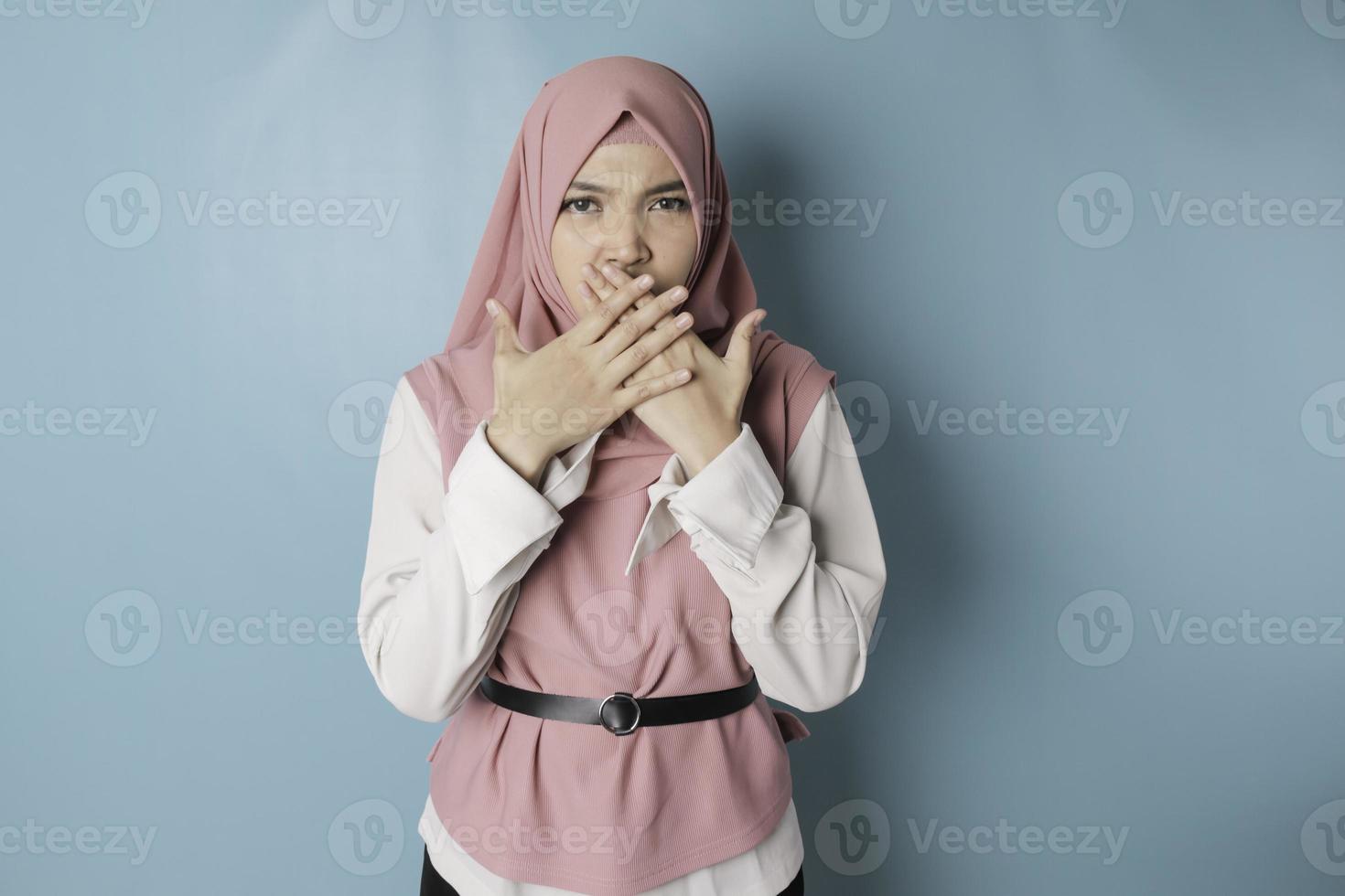 Surprised Asian Muslim woman wearing pink hijab isolated by blue background photo