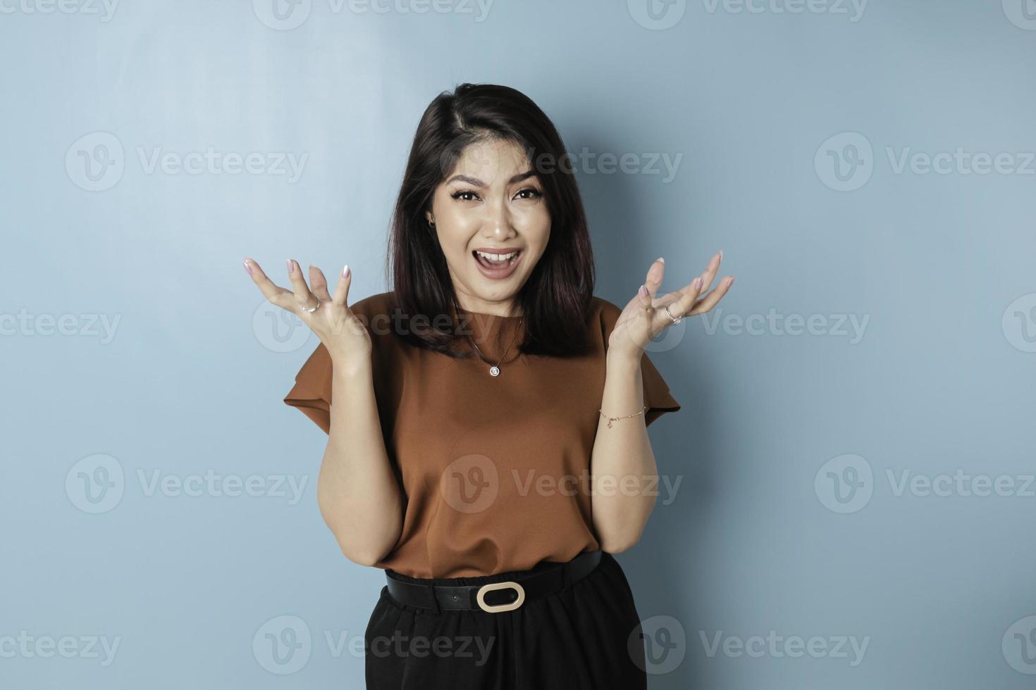 The angry and mad face of Asian woman in brown shirt on isolated blue background. photo