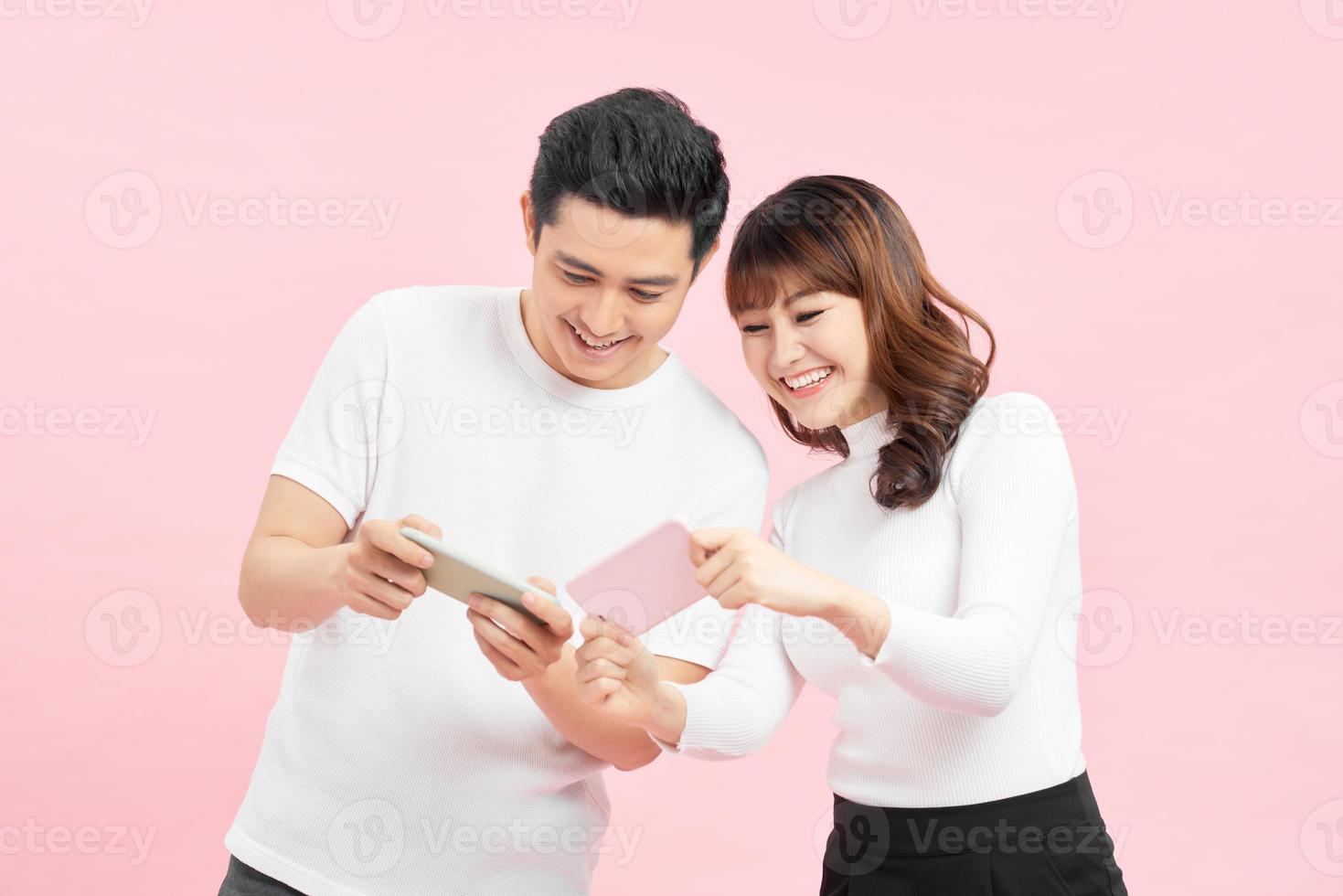 Image of funny young couple man and woman peeking at each others cell phones holding in hands isolated over pink background photo