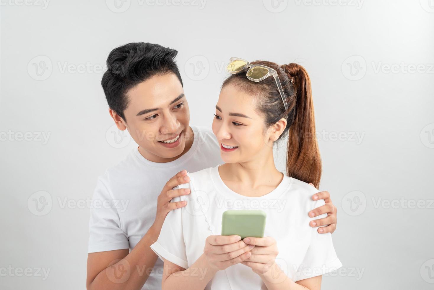 Curious boyfriend is spying his lovers smartphone. They are wearing casual shirts, standing isolated on white background photo