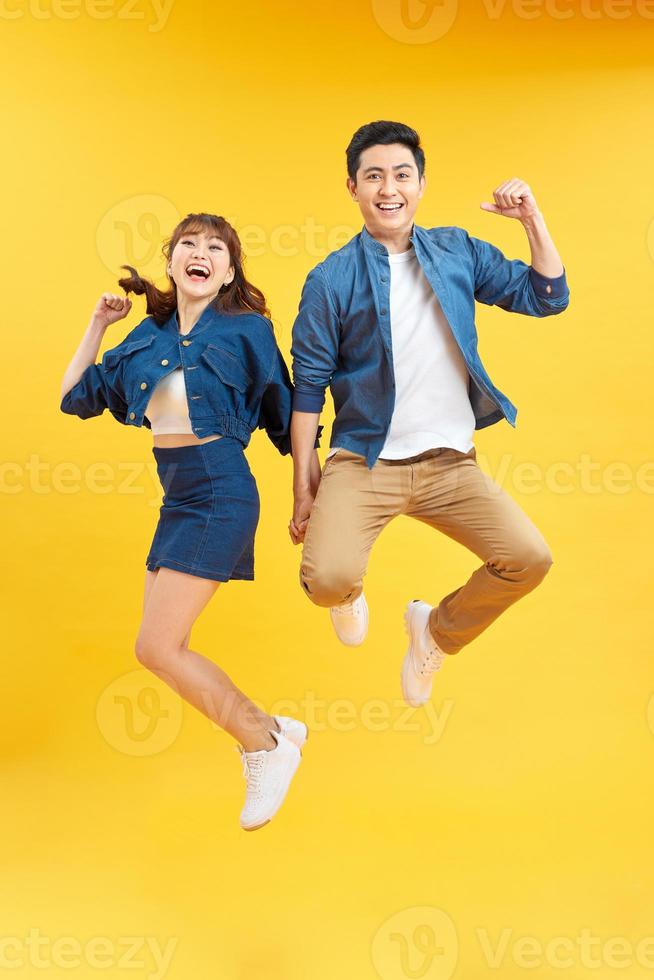 Full length portrait of amazed couple man and woman in basic t-shirts rejoicing while clenching fists isolated over yellow background photo