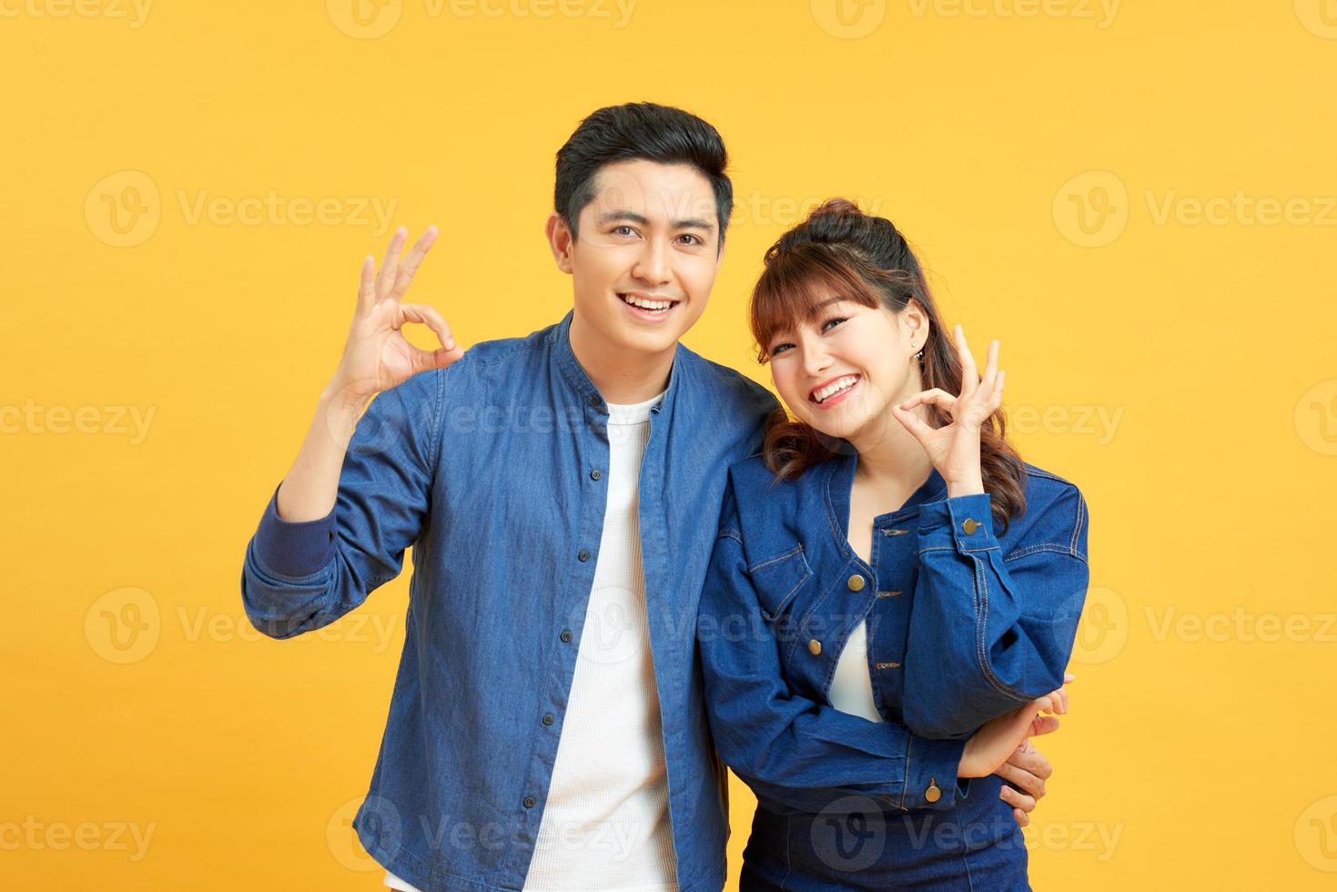 Beautiful young couple together standing over isolated yellow background looking surprised and shocked doing ok approval symbol with fingers. Crazy expression photo