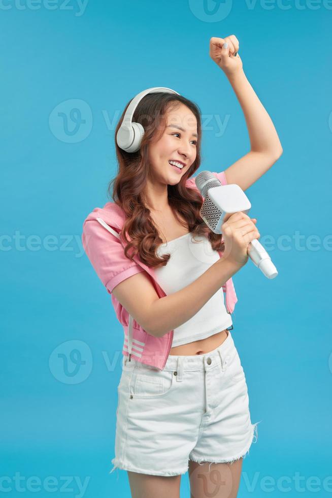 Young happy and excited Asian girl singing online karaoke song with microphone and jumping photo