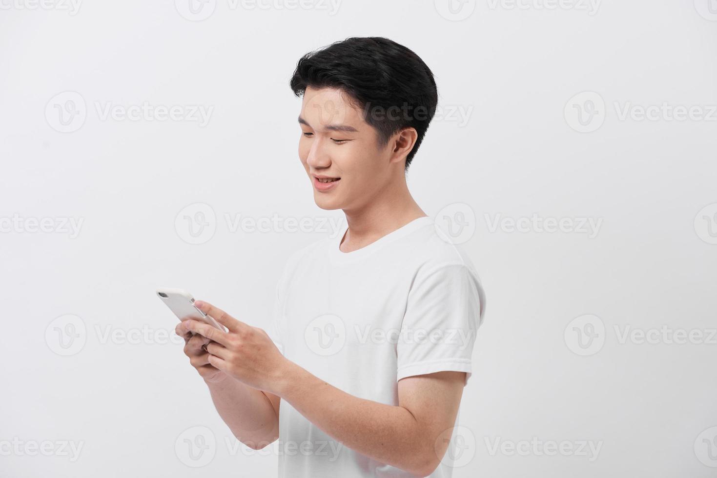 Handsome smiling man in white t-shirt holding smartphone and typing sms. photo