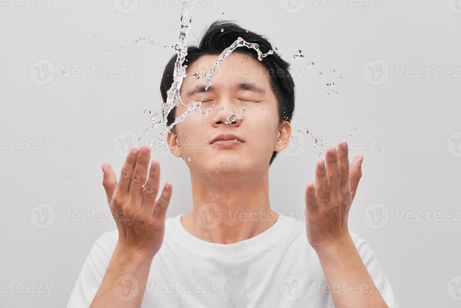 Young man spraying water on his face over gray background photo