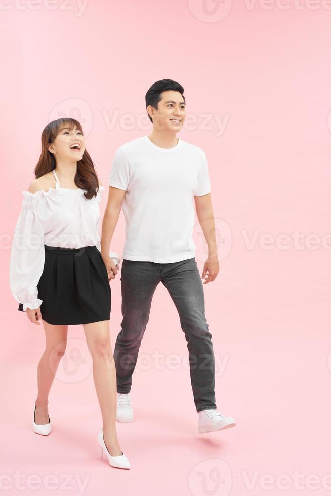 full length portrait of happy couple in casual outfit walking forward together on pink background photo