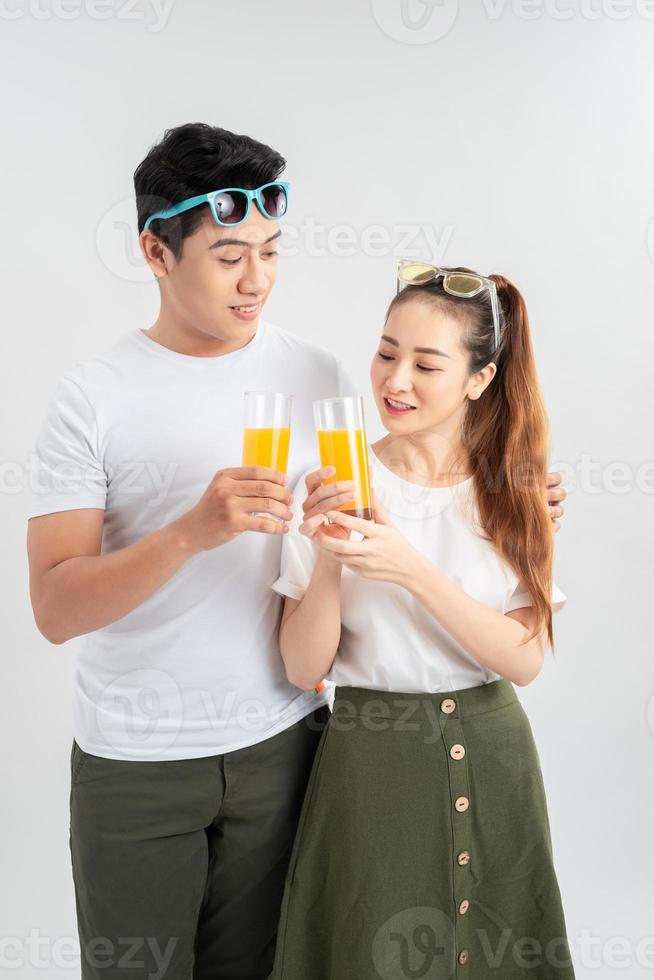 hermosa pareja joven de pie aislada sobre fondo blanco, sosteniendo vasos con jugo de naranja foto