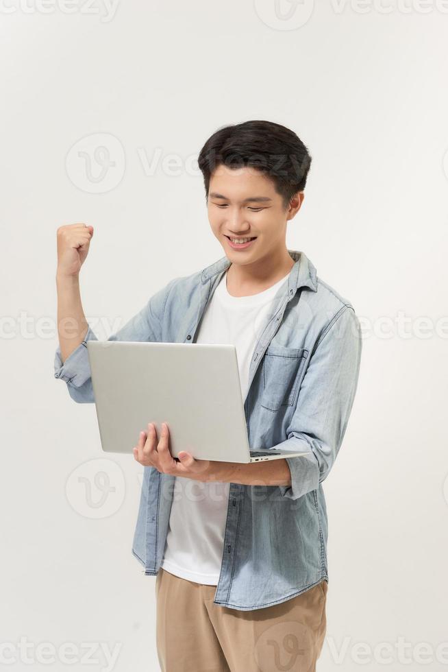 Happy young Asian man carrying laptop computer and raising his fist doing yes gesture isolated on white background photo