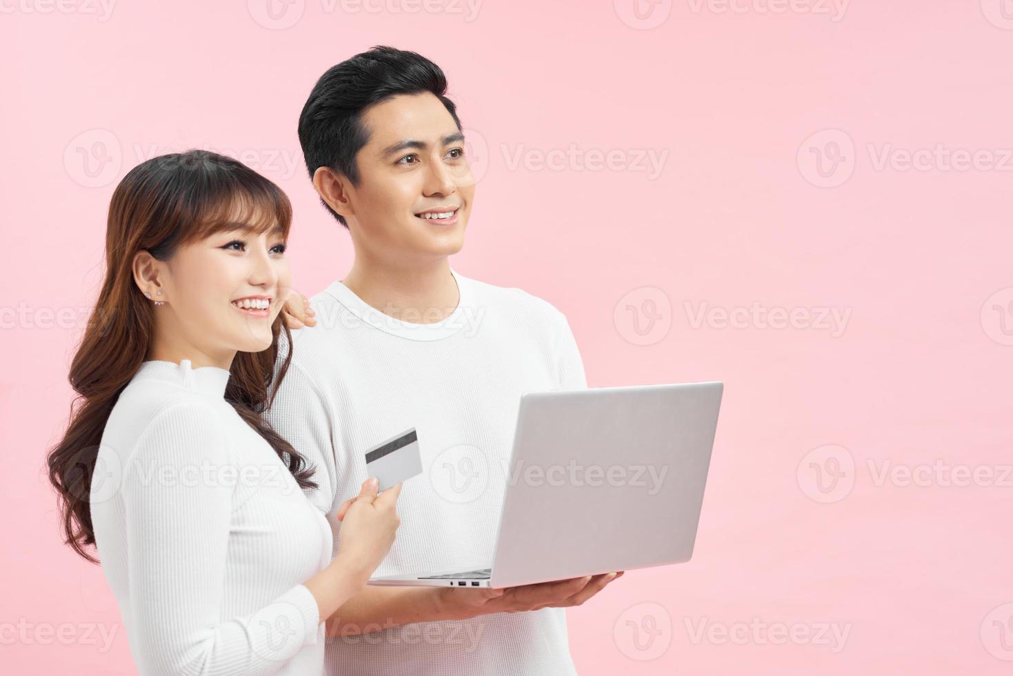 Excited young couple shopping online, holding credit card and looking at laptop photo