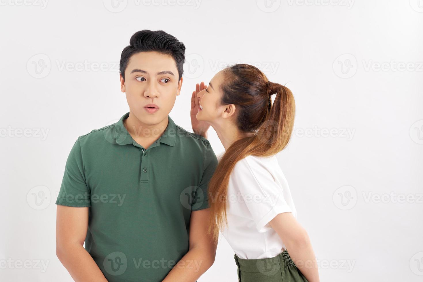 Portrait of attractive woman talking to handsome man in his ear isolated over white background photo