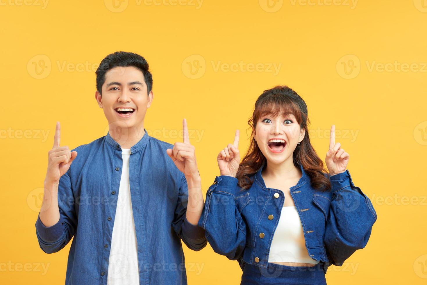 Young beautiful couple standing over isolated yellow background amazed and surprised looking up and pointing with fingers and raised arms. photo