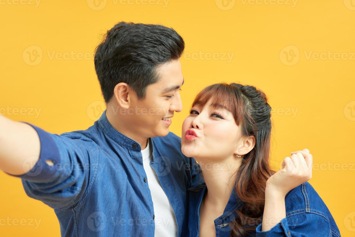 Portrait of two joyful people man and woman smiling while taking selfie photo isolated over yellow background