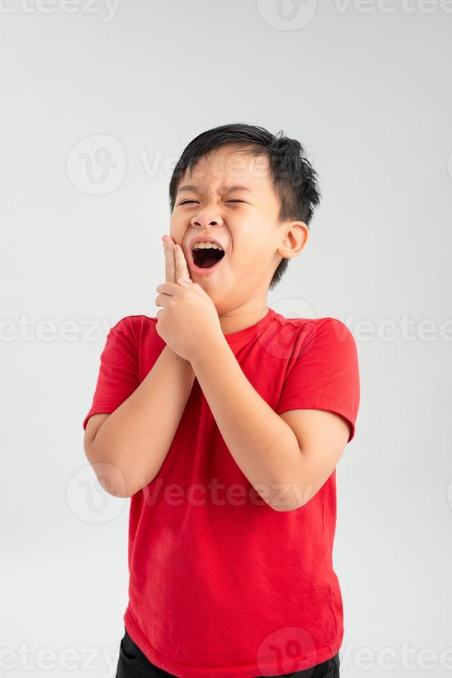 niño pequeño aspecto asiático en una camisa roja una mano en la mejilla cara arrugada sobre un fondo blanco, dolor de muelas retro foto