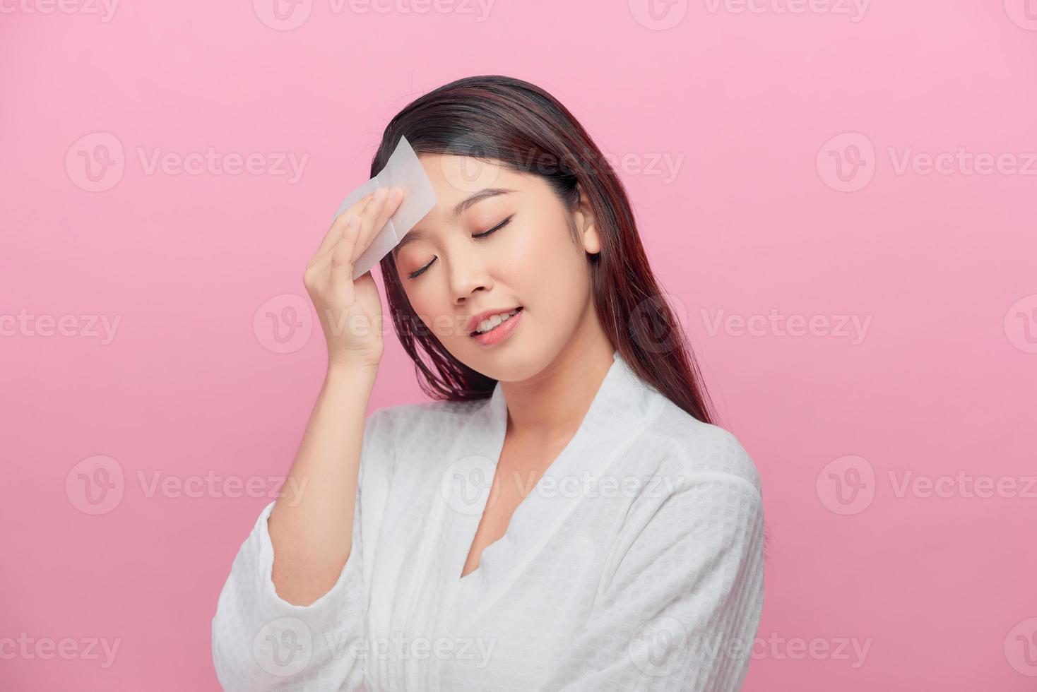 Young asian skin care woman smile and use oil blotting paper on her face photo