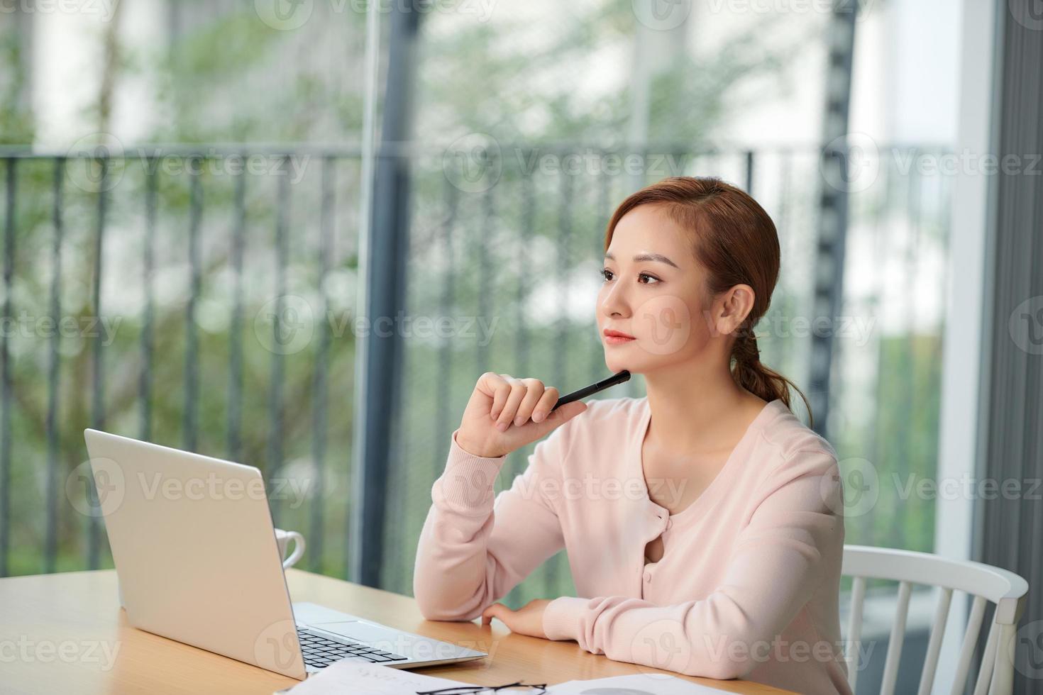 Smiling woman sitting alone in cafe near the bright window and working on laptop photo