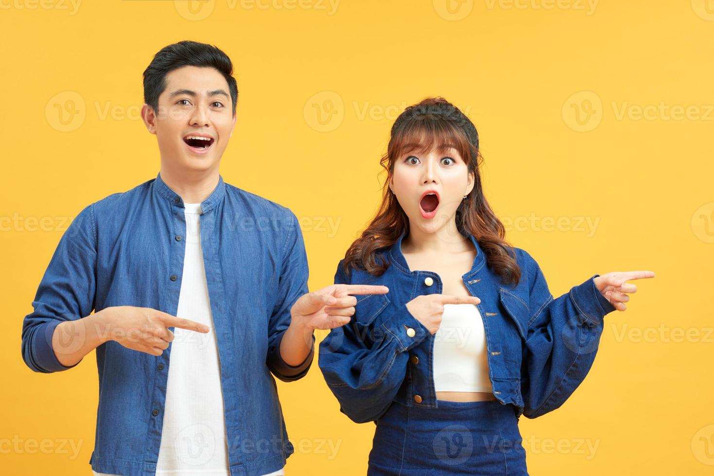 Young couple posing in a yellow background pointing to the side photo