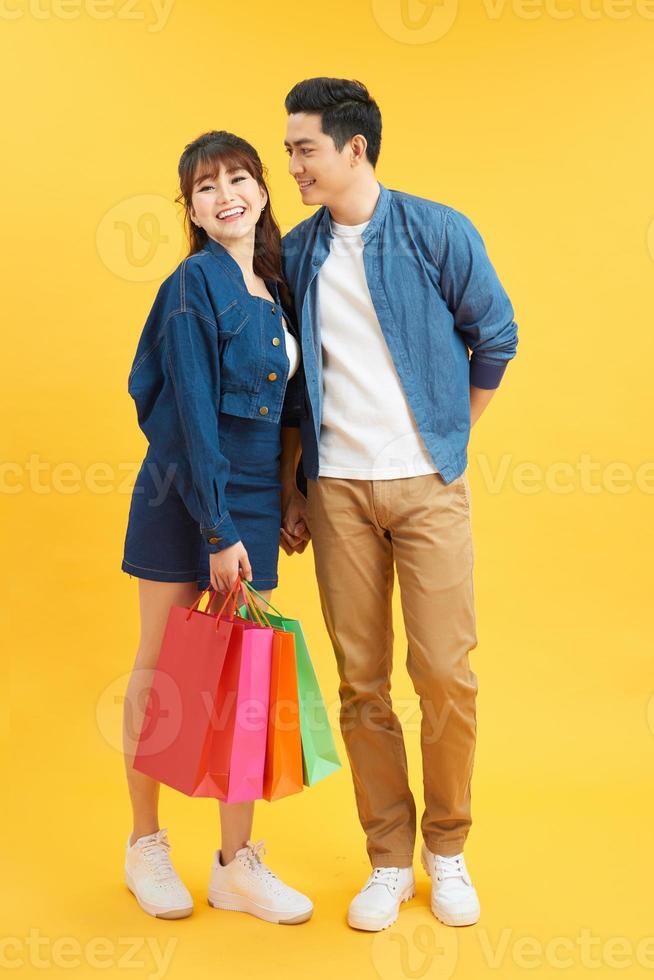 feliz pareja joven con bolsas de compras abrazándose y mirándose aislados en amarillo foto