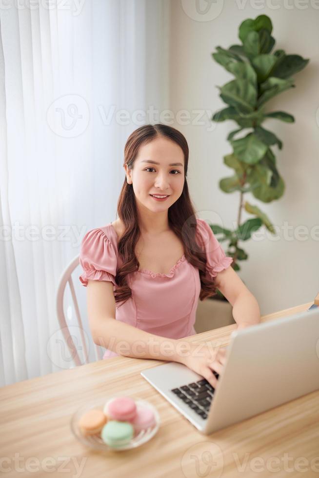 Smiling Asian woman using laptop at home. Freelancer. photo