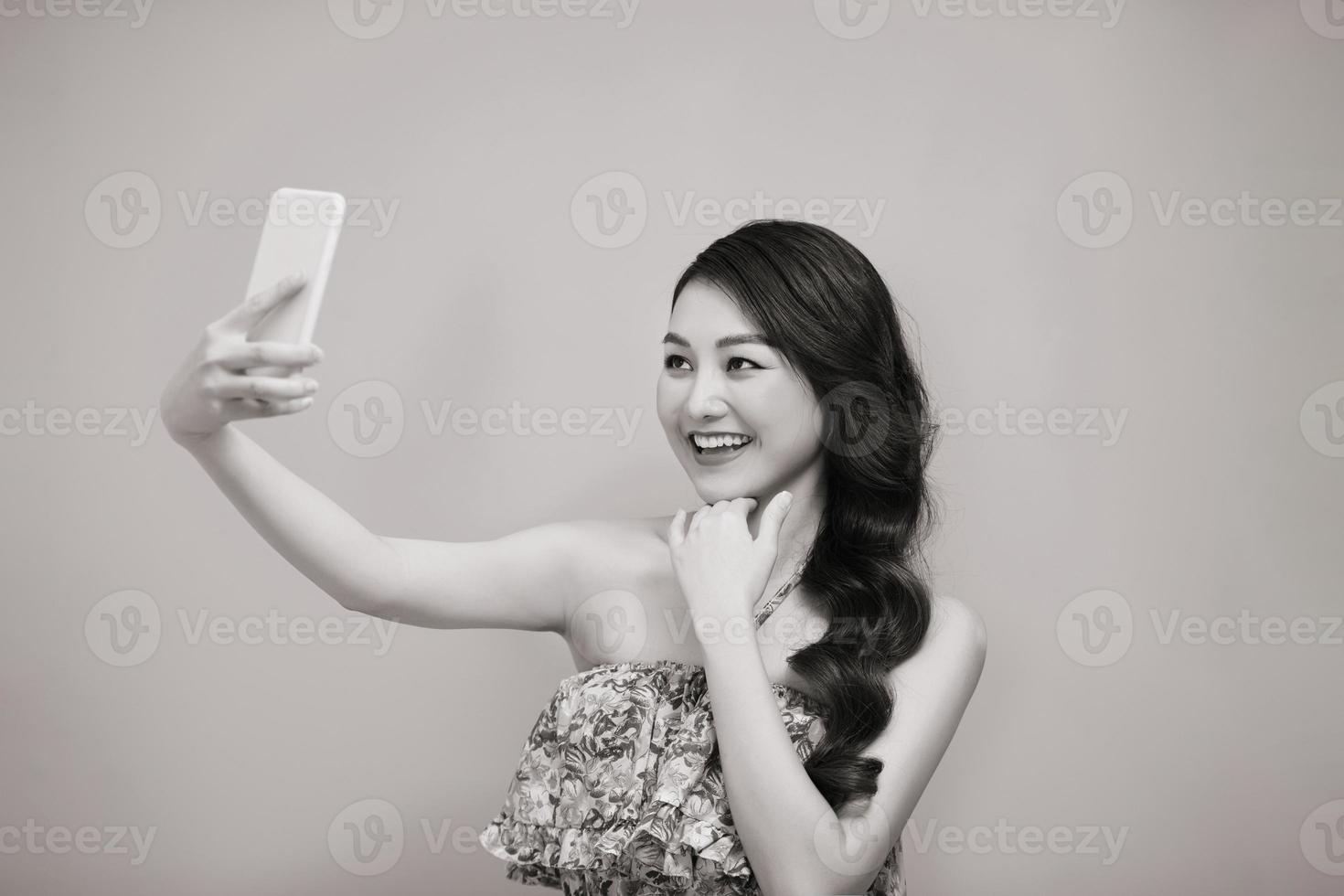 mujer joven tomando una foto selfie en un teléfono inteligente mirando la cámara riéndose feliz. foto en blanco y negro