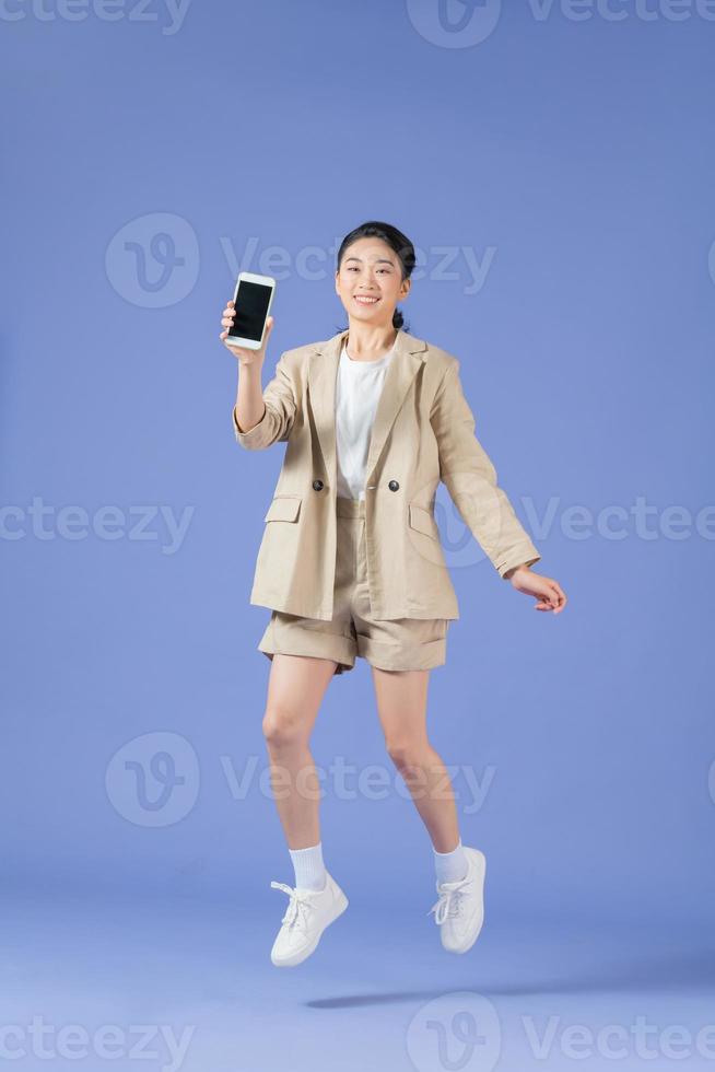 Cheerful girl jumping up and newest smartphone showing empty screen, enjoying new application for mobile phone photo